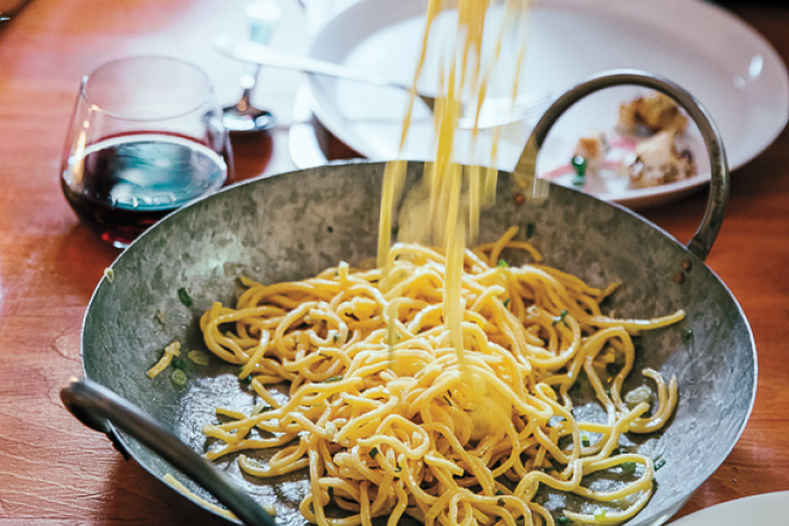 Wine glass next to a wok full of noodles